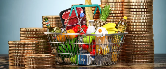 foto de uma cesta de alimentos e várias pilhas de moeda atrás  